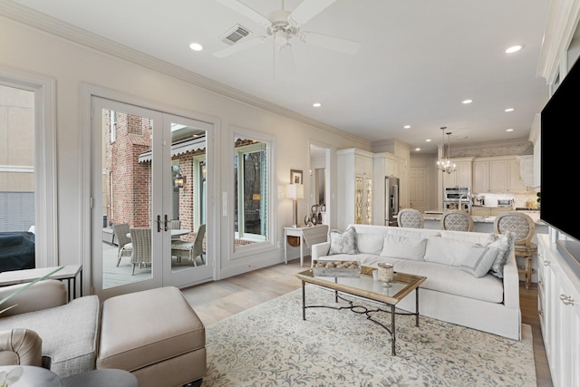 living area featuring visible vents, ceiling fan with notable chandelier, light wood-style flooring, and ornamental molding