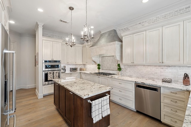 kitchen with visible vents, crown molding, premium range hood, appliances with stainless steel finishes, and an inviting chandelier