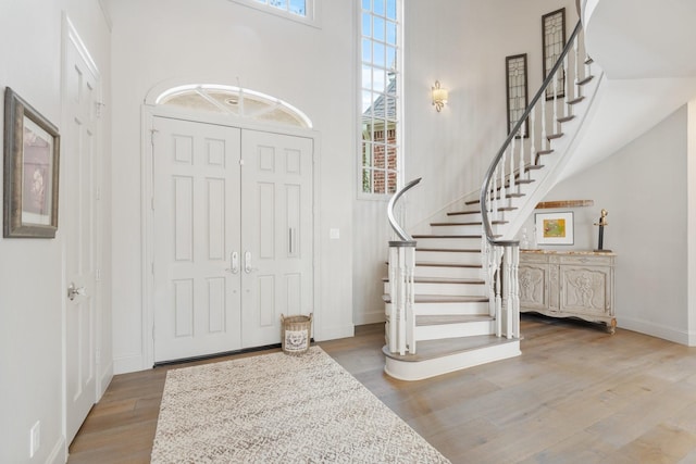 foyer entrance with stairway, wood finished floors, baseboards, and a towering ceiling