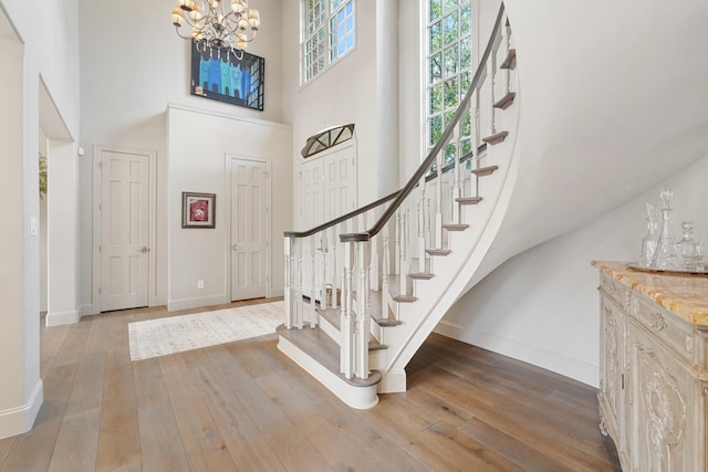 entrance foyer with wood-type flooring, a chandelier, baseboards, a towering ceiling, and stairs