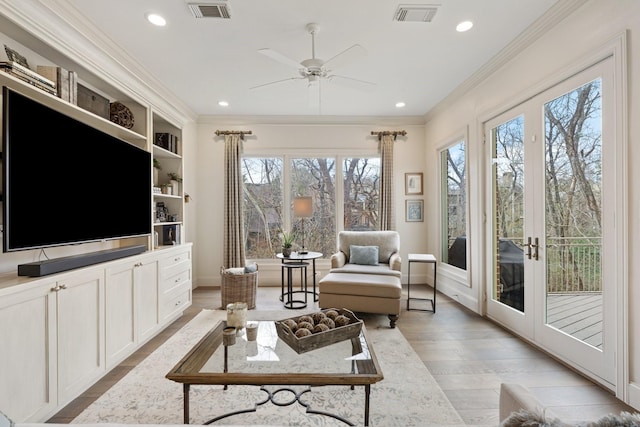 living area with crown molding, light wood-style flooring, visible vents, and ceiling fan