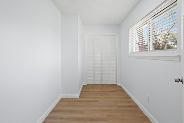 hall with baseboards, light wood finished floors, and a textured ceiling