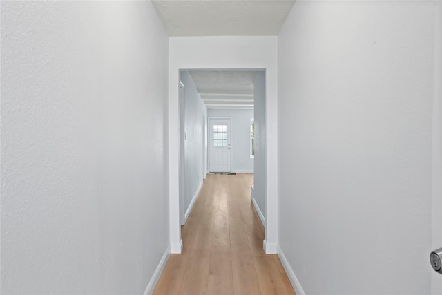 hallway featuring baseboards, a textured ceiling, and light wood-style flooring