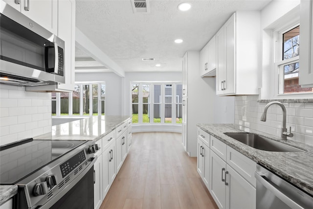 kitchen with a sink, light stone countertops, white cabinetry, and stainless steel appliances