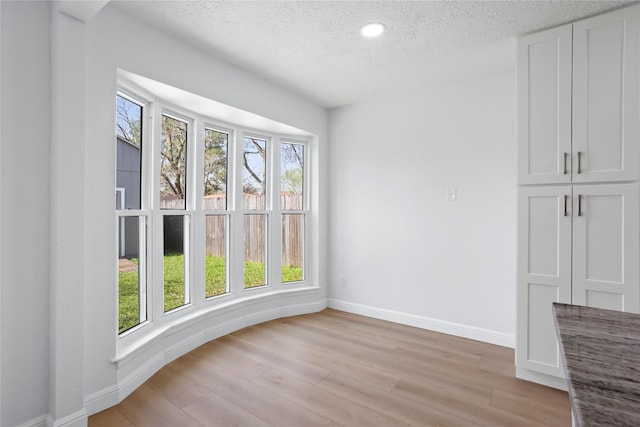 spare room with light wood-style flooring, a textured ceiling, and baseboards