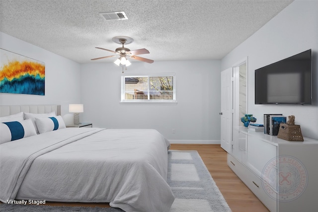 bedroom with visible vents, light wood-style floors, ceiling fan, and a textured ceiling