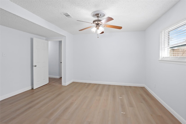 empty room with a ceiling fan, visible vents, light wood finished floors, baseboards, and a textured ceiling