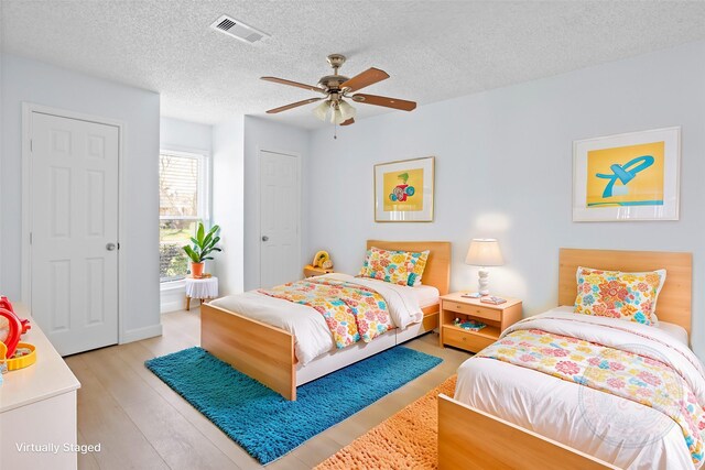 bedroom with visible vents, a textured ceiling, light wood-type flooring, and ceiling fan