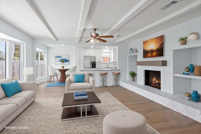 living area featuring a fireplace, visible vents, light wood finished floors, and a textured ceiling