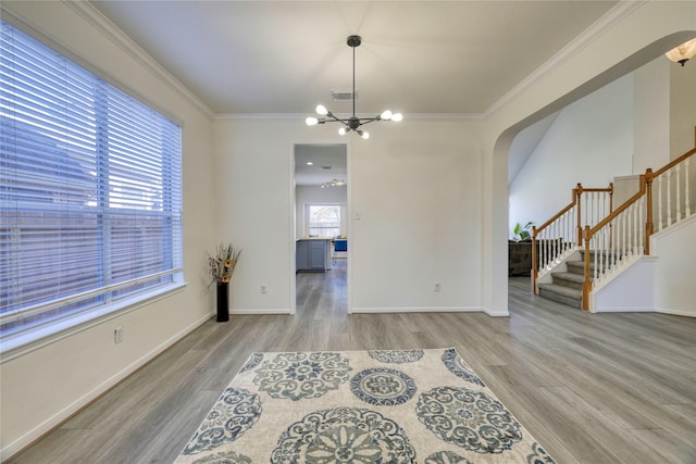 empty room featuring visible vents, ornamental molding, wood finished floors, arched walkways, and stairs