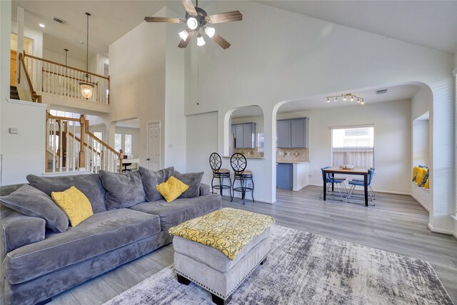 living room featuring visible vents, ceiling fan, stairway, light wood-type flooring, and arched walkways