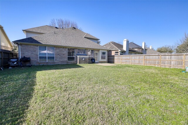 rear view of house with a lawn, roof with shingles, a fenced backyard, and brick siding