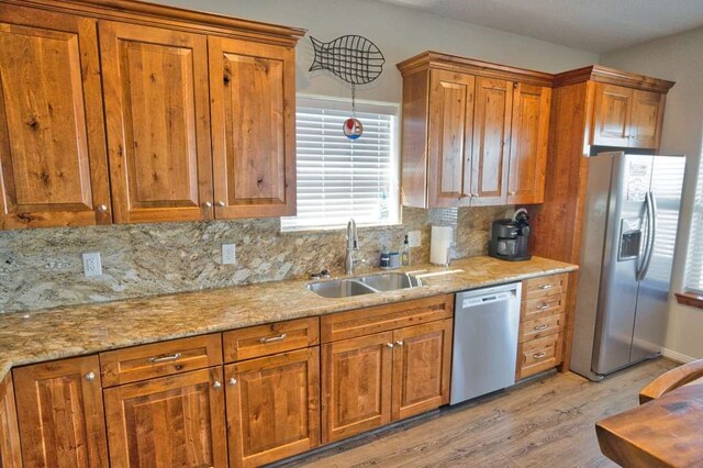 kitchen with brown cabinetry, light wood finished floors, appliances with stainless steel finishes, and a sink