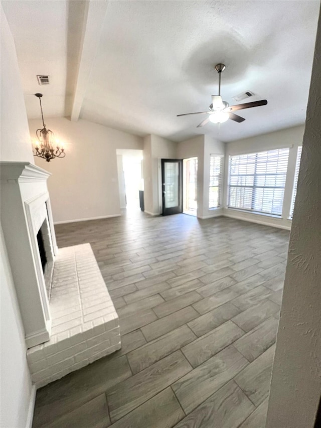 unfurnished living room featuring wood finished floors, visible vents, lofted ceiling with beams, a fireplace, and ceiling fan with notable chandelier