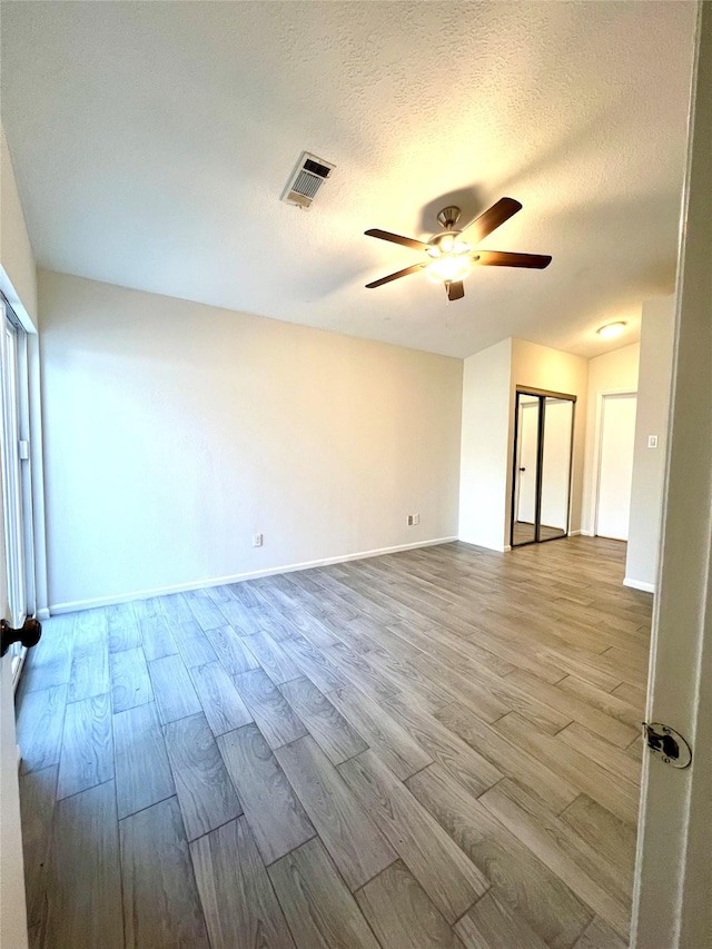 unfurnished room with wood finished floors, a ceiling fan, visible vents, and a textured ceiling