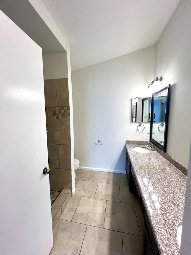 bathroom featuring tile patterned flooring, baseboards, toilet, a tile shower, and vanity