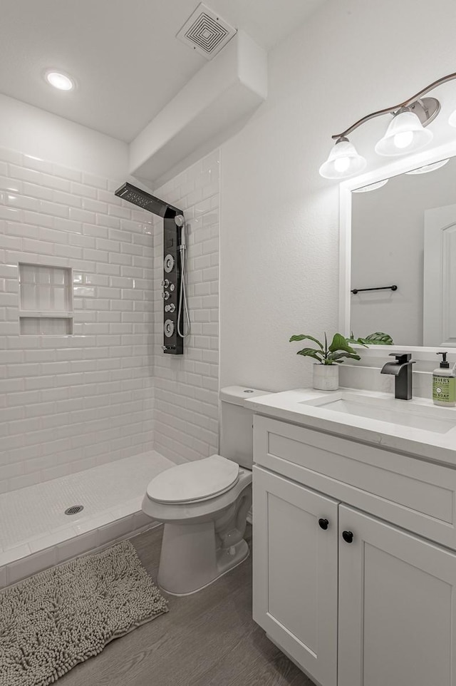 full bath featuring vanity, wood finished floors, visible vents, a tile shower, and toilet