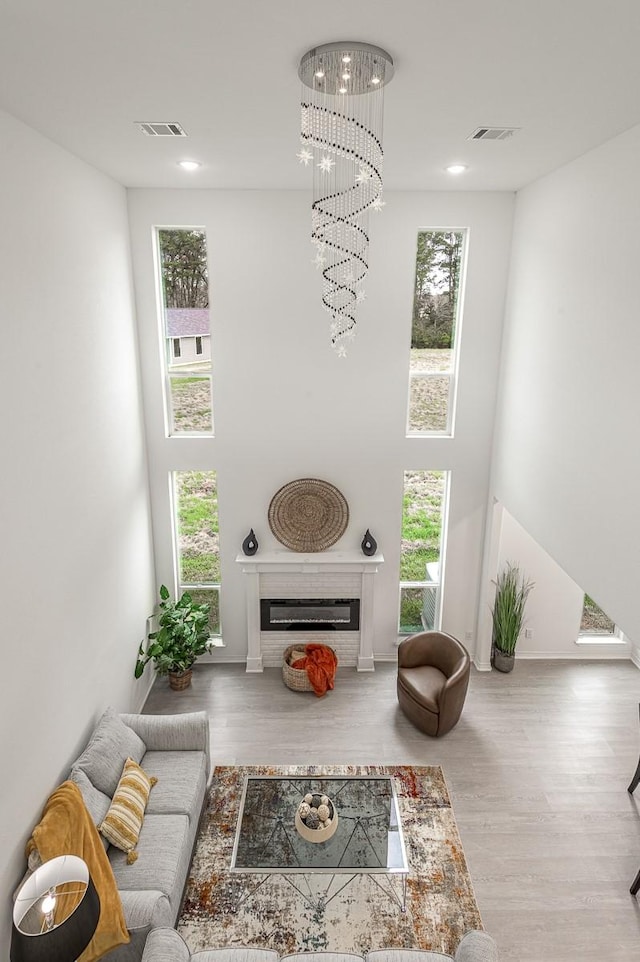 living room featuring visible vents, a chandelier, a high ceiling, wood finished floors, and a glass covered fireplace