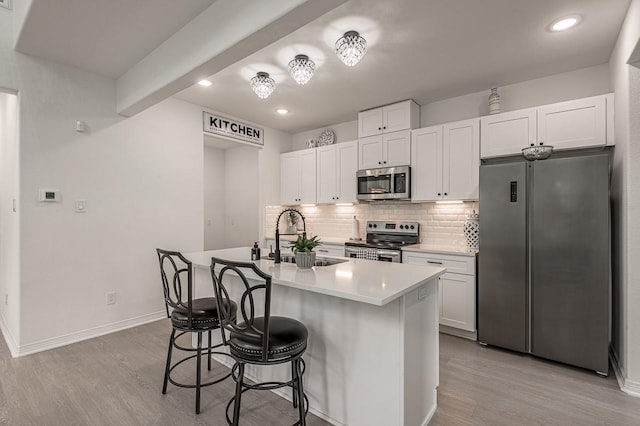 kitchen with a breakfast bar area, light wood finished floors, a sink, decorative backsplash, and stainless steel appliances