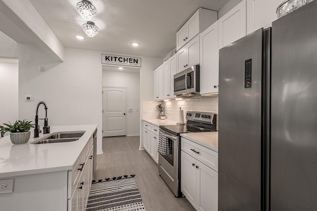 kitchen featuring tasteful backsplash, light wood-type flooring, appliances with stainless steel finishes, white cabinets, and a sink