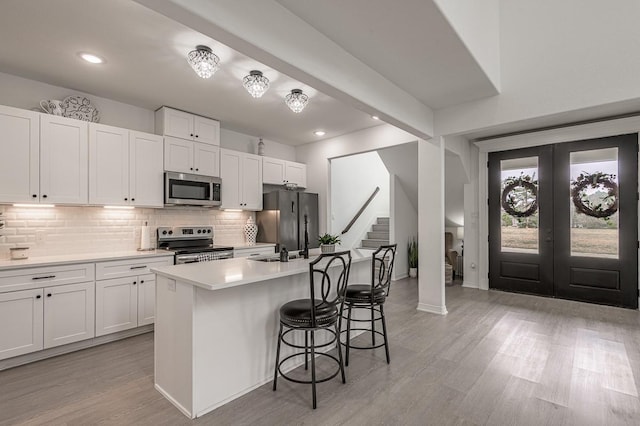 kitchen with light wood-style floors, backsplash, appliances with stainless steel finishes, and a breakfast bar area