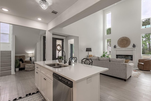 kitchen with visible vents, open floor plan, stainless steel dishwasher, a glass covered fireplace, and a sink