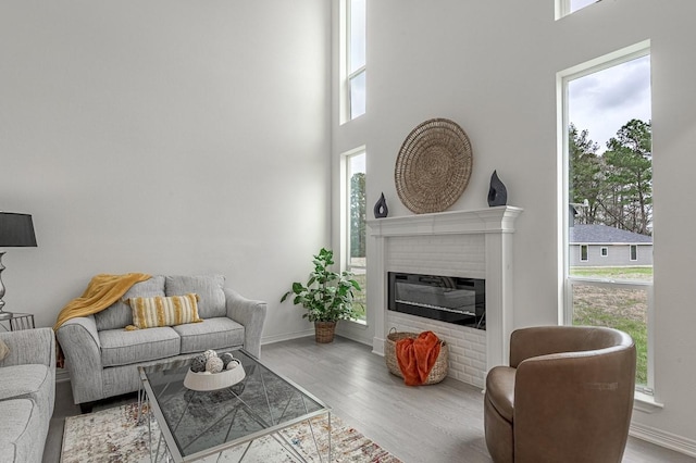 living area featuring baseboards, a high ceiling, a brick fireplace, and wood finished floors