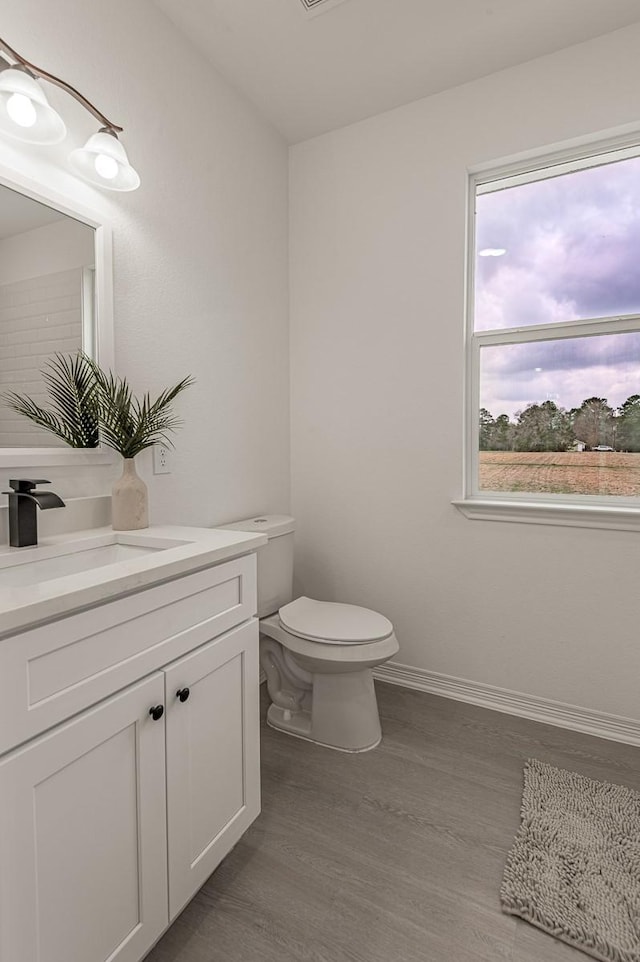 half bathroom with vanity, toilet, wood finished floors, and baseboards