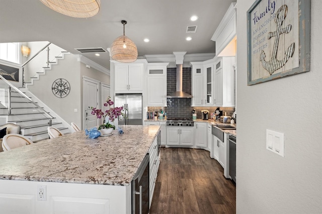 kitchen featuring visible vents, wall chimney range hood, light stone counters, appliances with stainless steel finishes, and white cabinetry