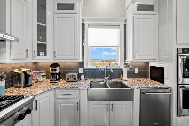 kitchen with decorative backsplash, white cabinets, wall chimney exhaust hood, and a sink