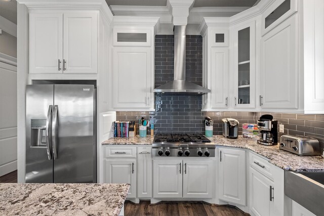 kitchen with backsplash, appliances with stainless steel finishes, wall chimney exhaust hood, and white cabinets