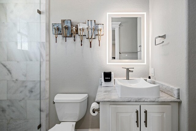 bathroom with vanity, a shower stall, toilet, and a textured wall