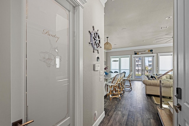 hallway featuring dark wood finished floors, visible vents, a textured wall, and ornamental molding