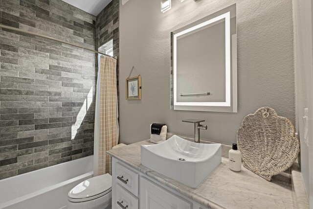 bathroom with vanity, toilet, shower / bathtub combination with curtain, and a textured wall