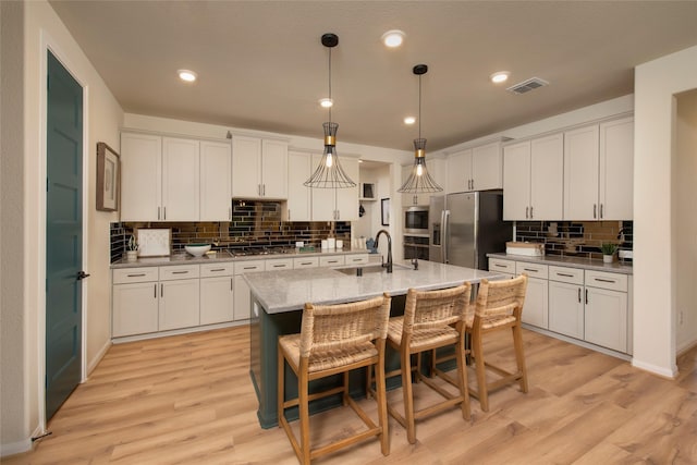 kitchen featuring visible vents, light wood-style flooring, appliances with stainless steel finishes, white cabinets, and a sink