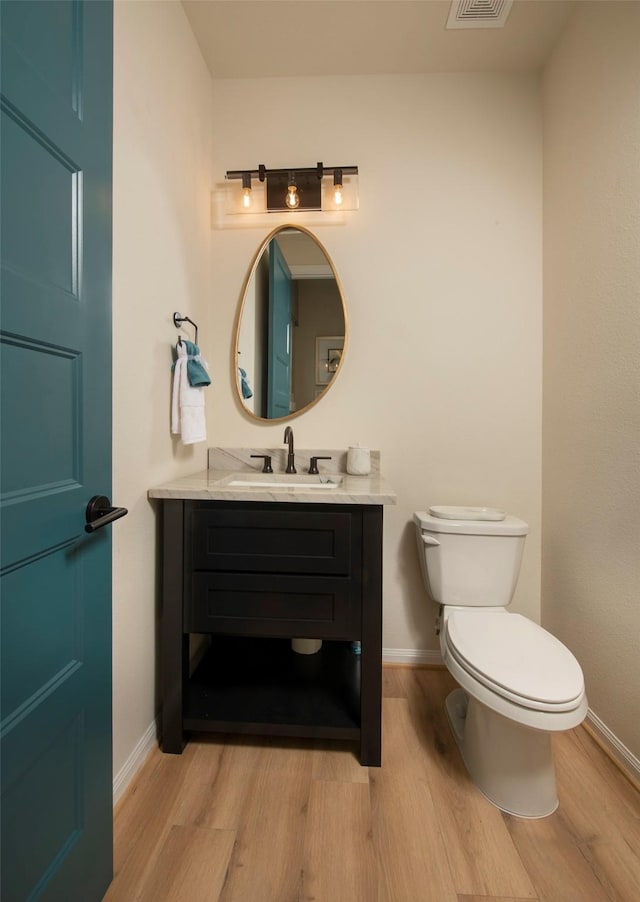 half bathroom with visible vents, baseboards, toilet, wood finished floors, and vanity