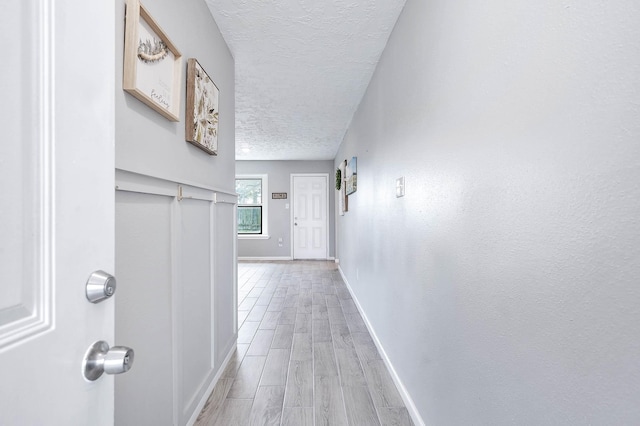 corridor featuring light wood-style flooring, a textured ceiling, and baseboards