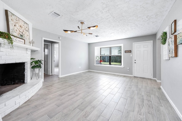 unfurnished living room featuring light wood finished floors, visible vents, a brick fireplace, and a textured ceiling