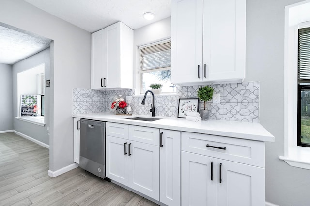 kitchen featuring backsplash, dishwasher, light countertops, white cabinets, and a sink