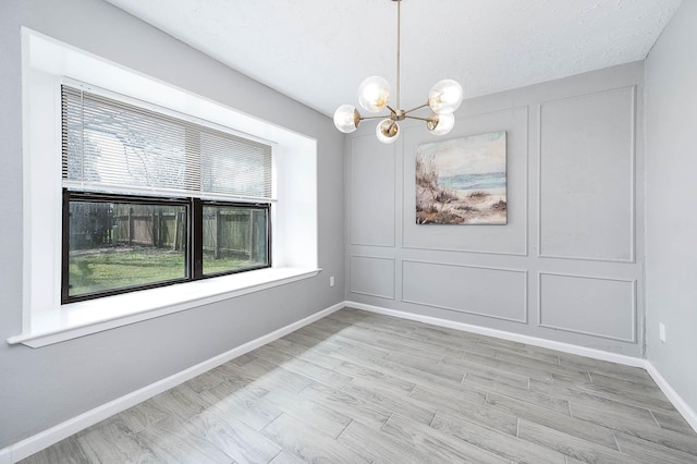 unfurnished dining area featuring baseboards, an inviting chandelier, wood finished floors, a decorative wall, and a textured ceiling