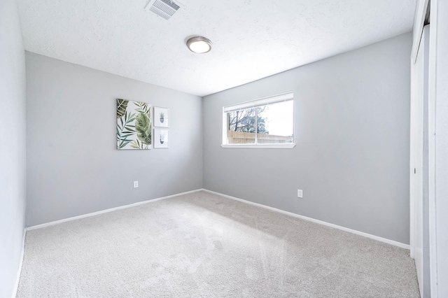 carpeted spare room featuring baseboards, visible vents, and a textured ceiling