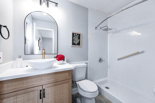 bathroom featuring a textured ceiling, walk in shower, vanity, and toilet