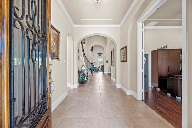 foyer entrance featuring arched walkways, light tile patterned floors, baseboards, and ornamental molding