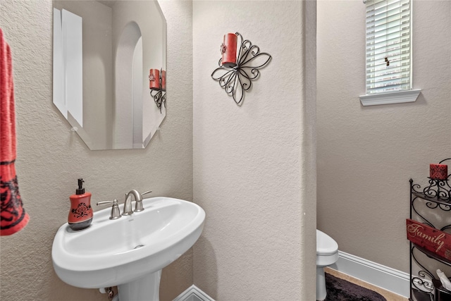 bathroom with a sink, baseboards, toilet, and a textured wall