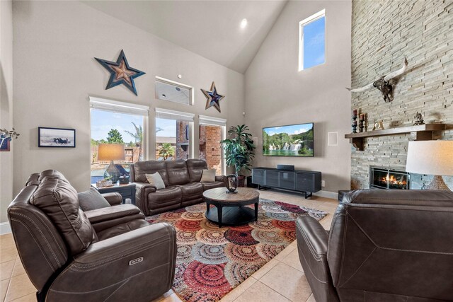 living area with light tile patterned floors, a stone fireplace, high vaulted ceiling, and baseboards