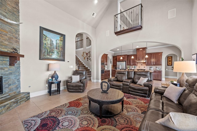 living room featuring baseboards, light tile patterned flooring, arched walkways, a stone fireplace, and a towering ceiling