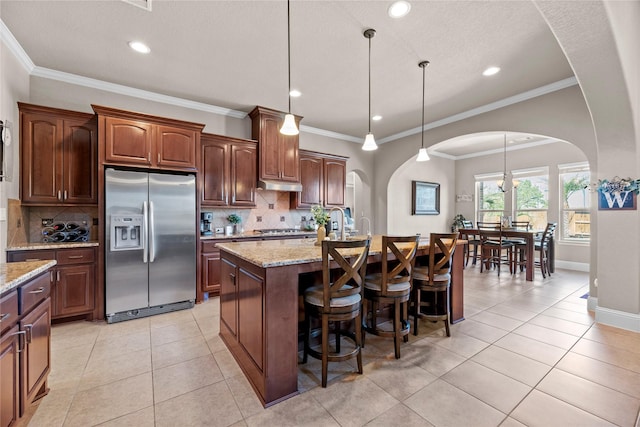 kitchen with a center island with sink, under cabinet range hood, arched walkways, appliances with stainless steel finishes, and light tile patterned flooring