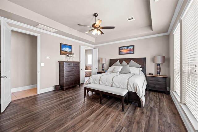 bedroom with dark wood-style floors, visible vents, baseboards, and a tray ceiling