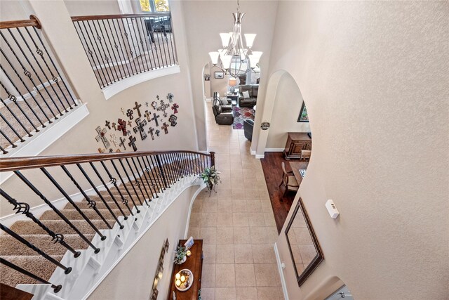 stairway with baseboards, arched walkways, a chandelier, and a towering ceiling