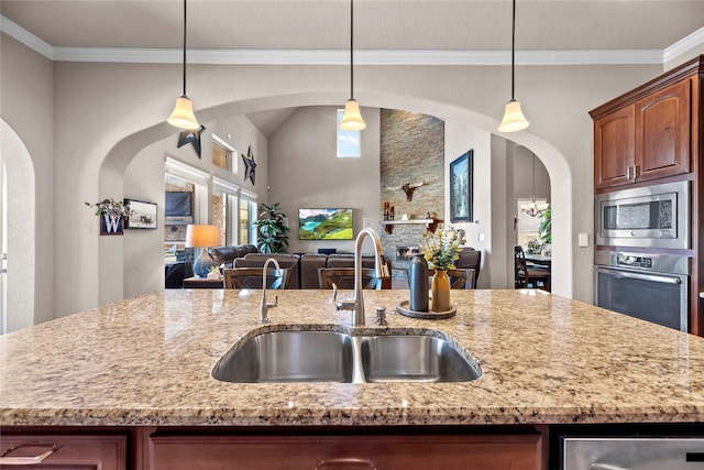 kitchen with light stone countertops, arched walkways, a sink, appliances with stainless steel finishes, and open floor plan